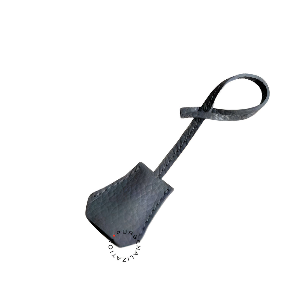 An image of a clochette leather charm for handbags accessories in the variety Aurore, a shade of grey with a hint of blue.
