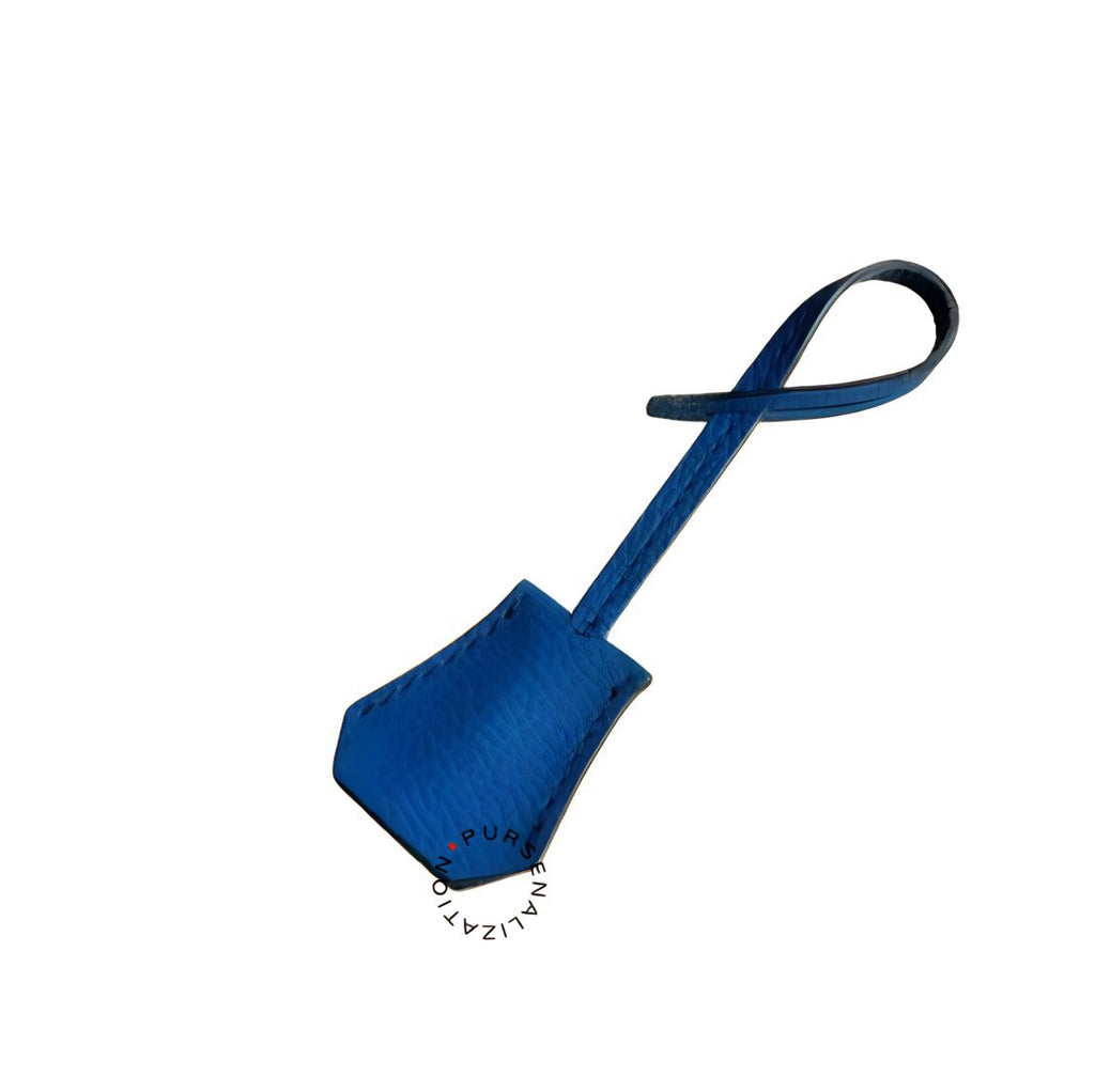 An image of a clochette leather charm for handbags accessories in the variety Comete, a shade of medium blue.